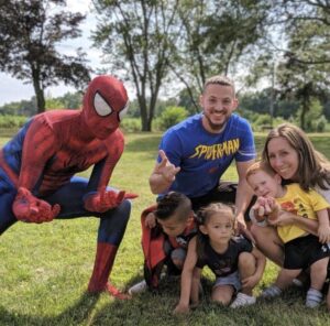 Spiderman performer posing with children at a birthday party, striking superhero poses.