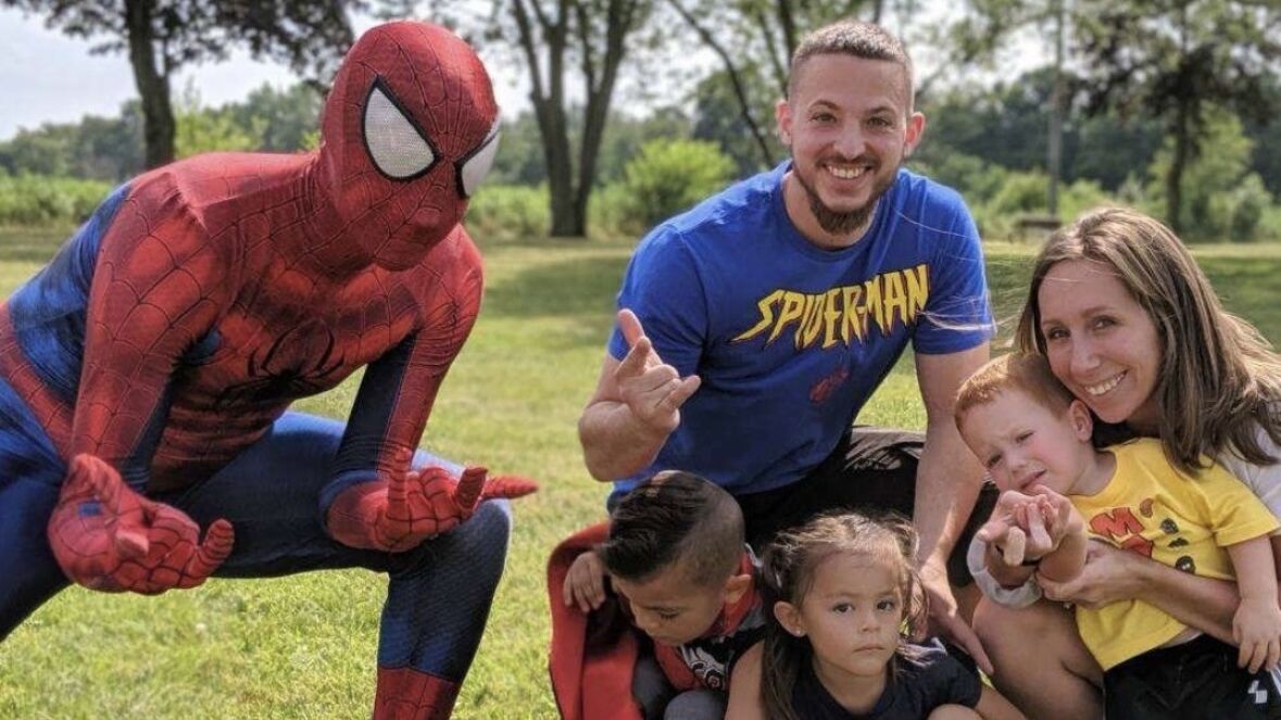 Spiderman performer posing with children at a birthday party, striking superhero poses.